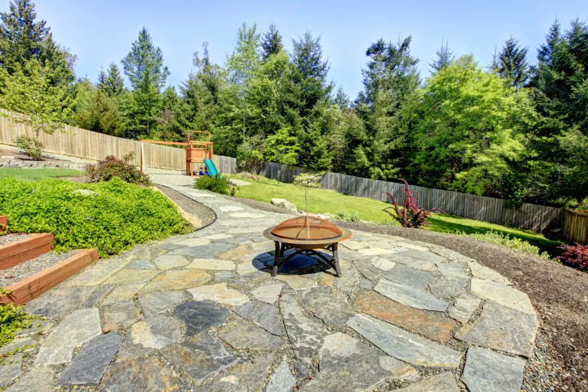 Metal fire pit with a cover inside a fenced yard.