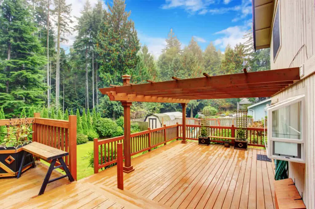 Spacious wooden deck with benches with an example of how pergolas add to  home  value.  