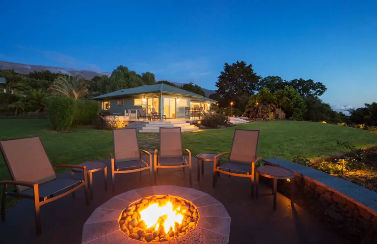 Outdoor fire pit with chairs surrounding it and a house in the background showing lighting your outdoor fire pit.