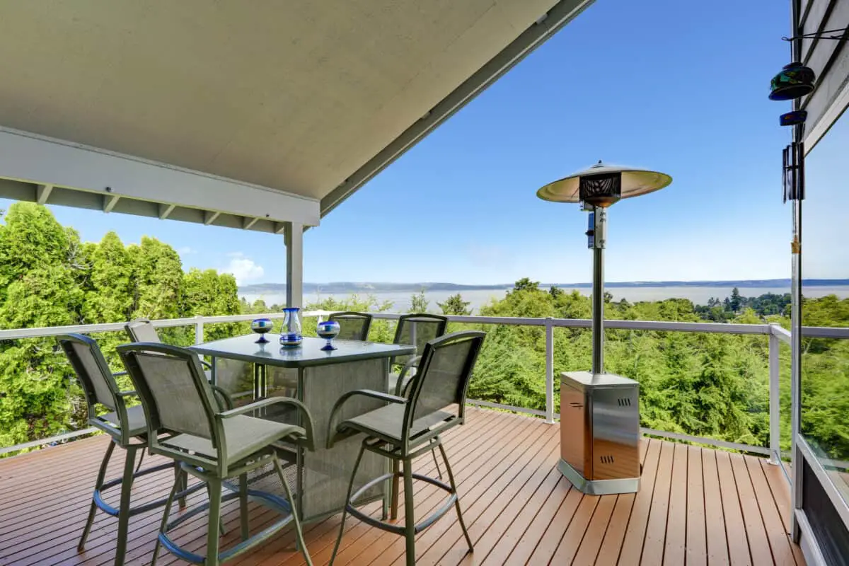 Patio heater with a tilt sensor to the side of chairs and table overlooking trees and lake showing patio heater safety.