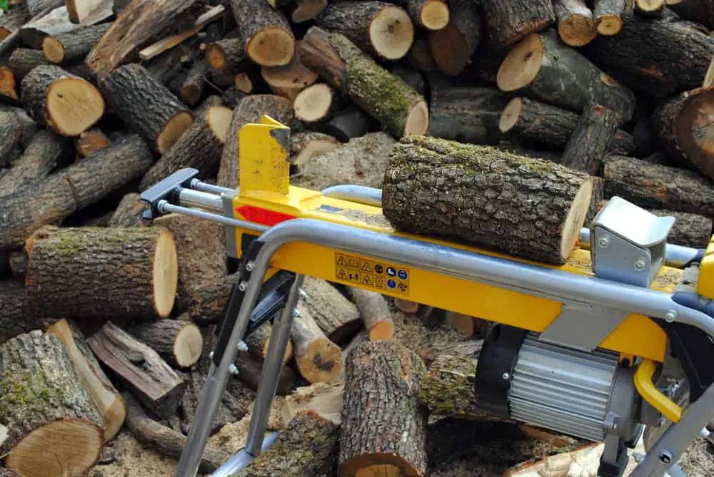 Close up of log splitter with a pile of logs in the background using a log splitter safely.