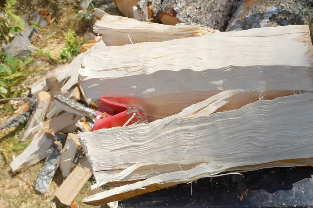 Wood being split using a DIY log splitter wedge, close up picture with stack of split wood in background.