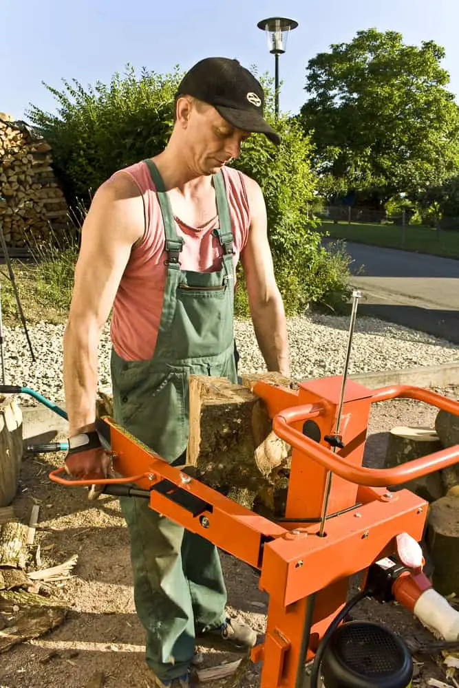 Man on driveway using heavy-duty log splitter to split a large piece of wood show difference between gas or electric log splitters.