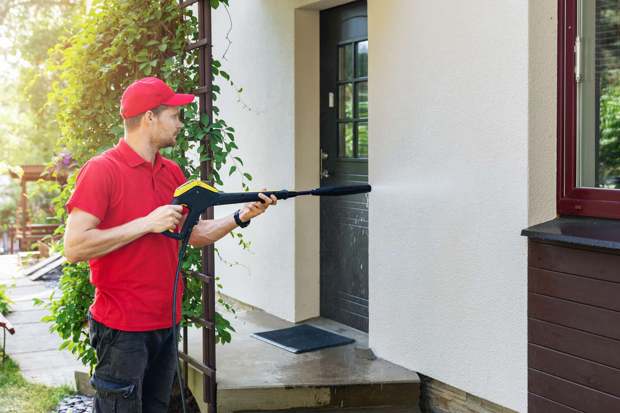 worker with high pressure washer cleaning house facade