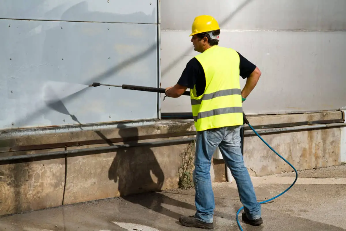 A man using pressure washer safety tips while cleaning a building.