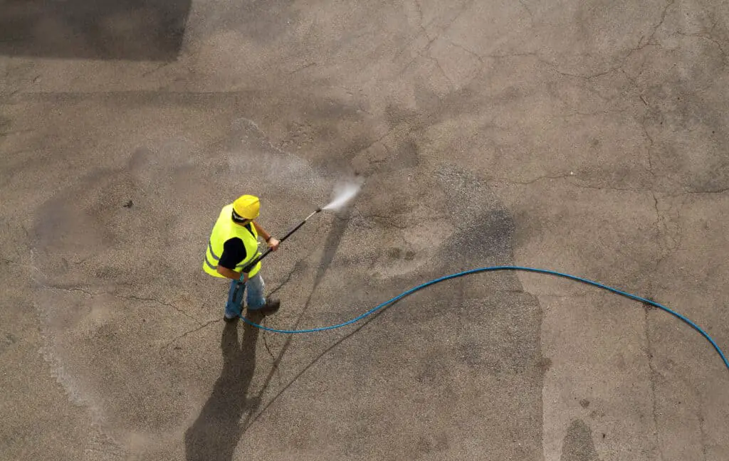 man wearing safety equipment pressure washing concrete using a 100 ft hose