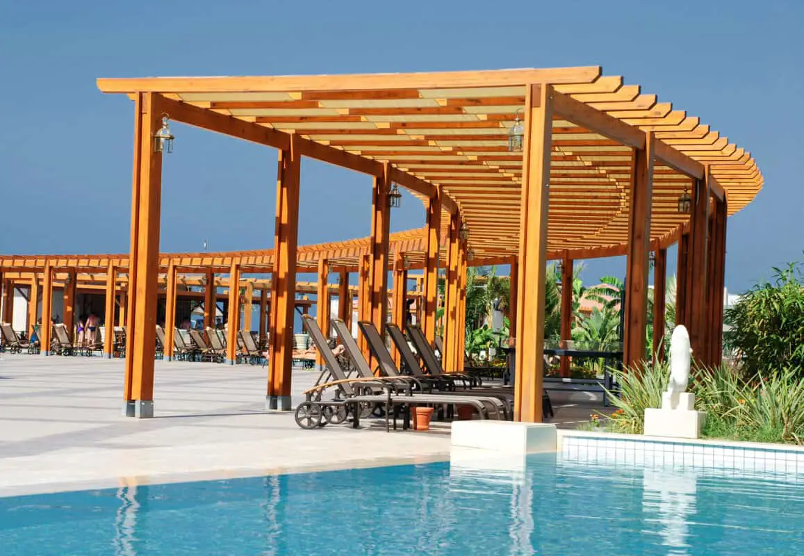 Wooden pergola next to swimming pool to block the sun showing the best wood for your pergola.