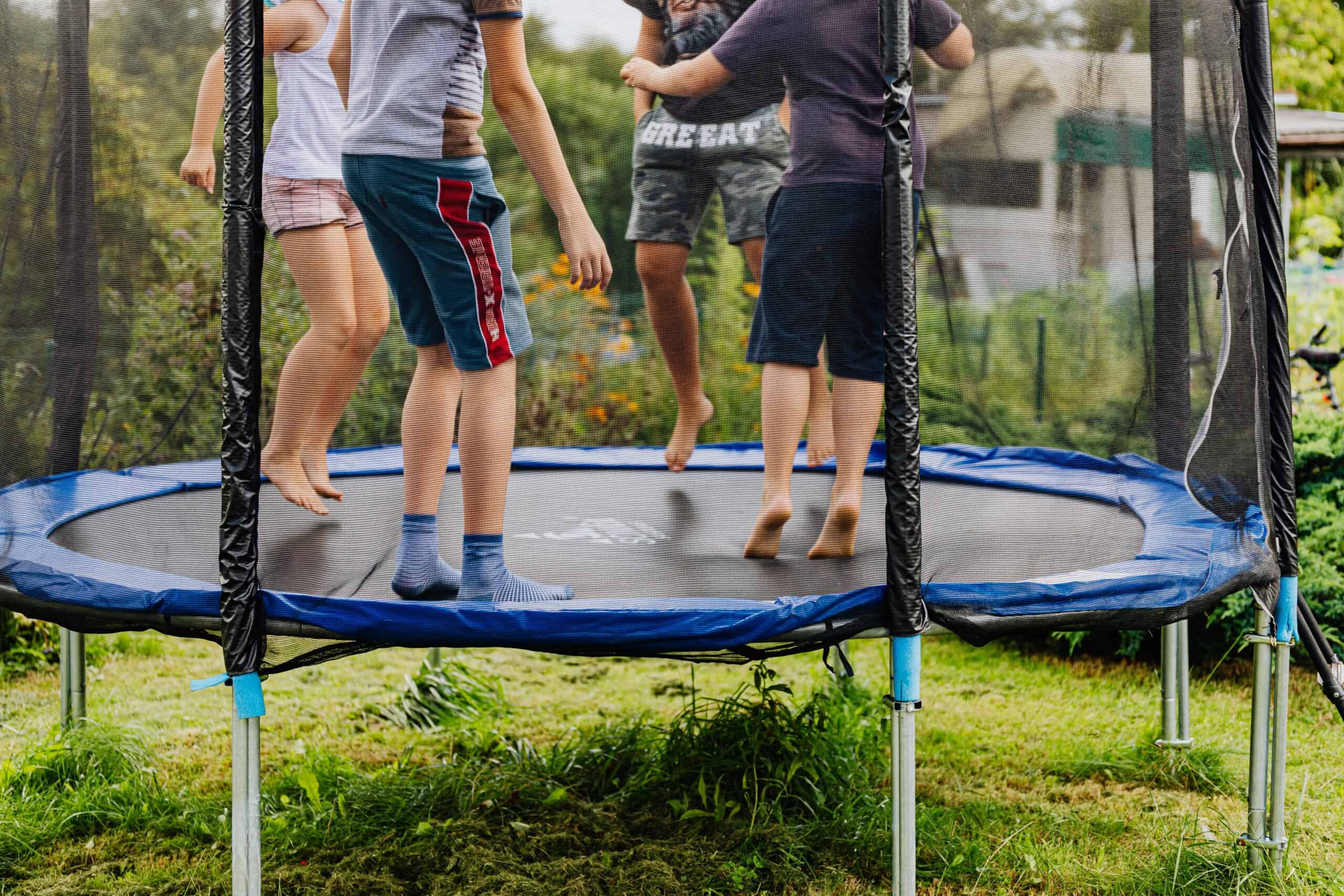 children jumping on trampoline with net in backyard outdoors