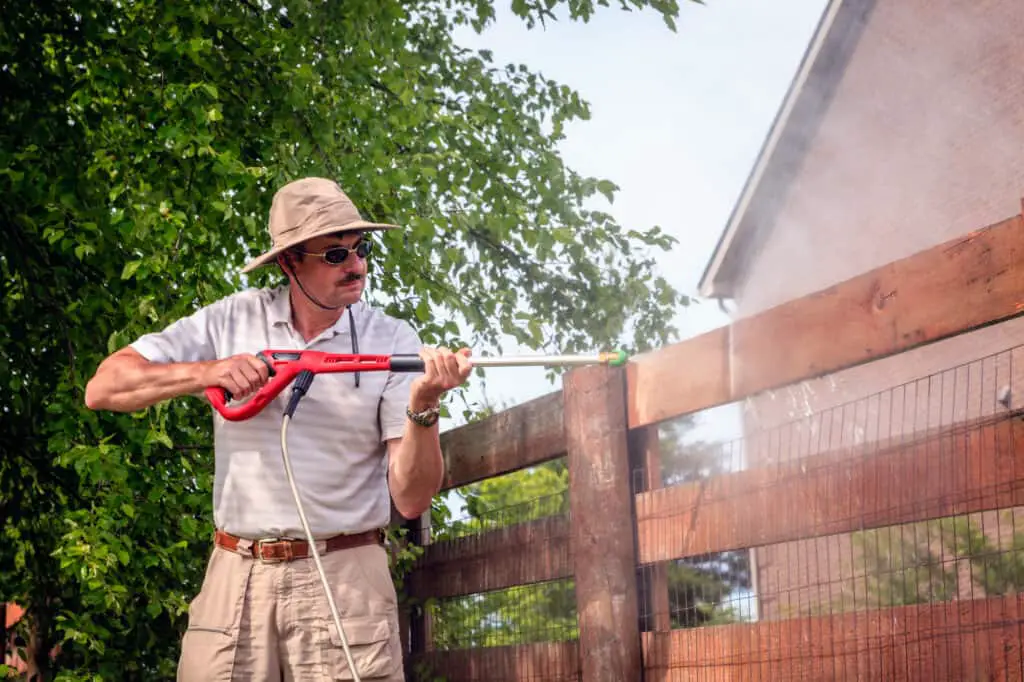 A man is cleaning wooden fence with electric power washer