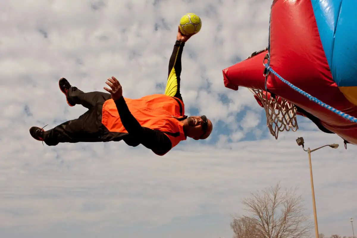 Man slam dunking basketball hoop on trampoline, but could be risk of common trampoline injuries.