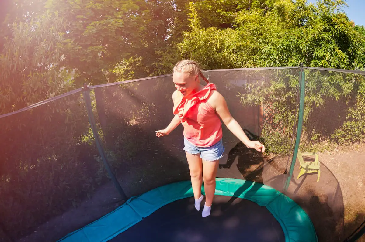 Girl jumping on a trampoline in backyard on concrete