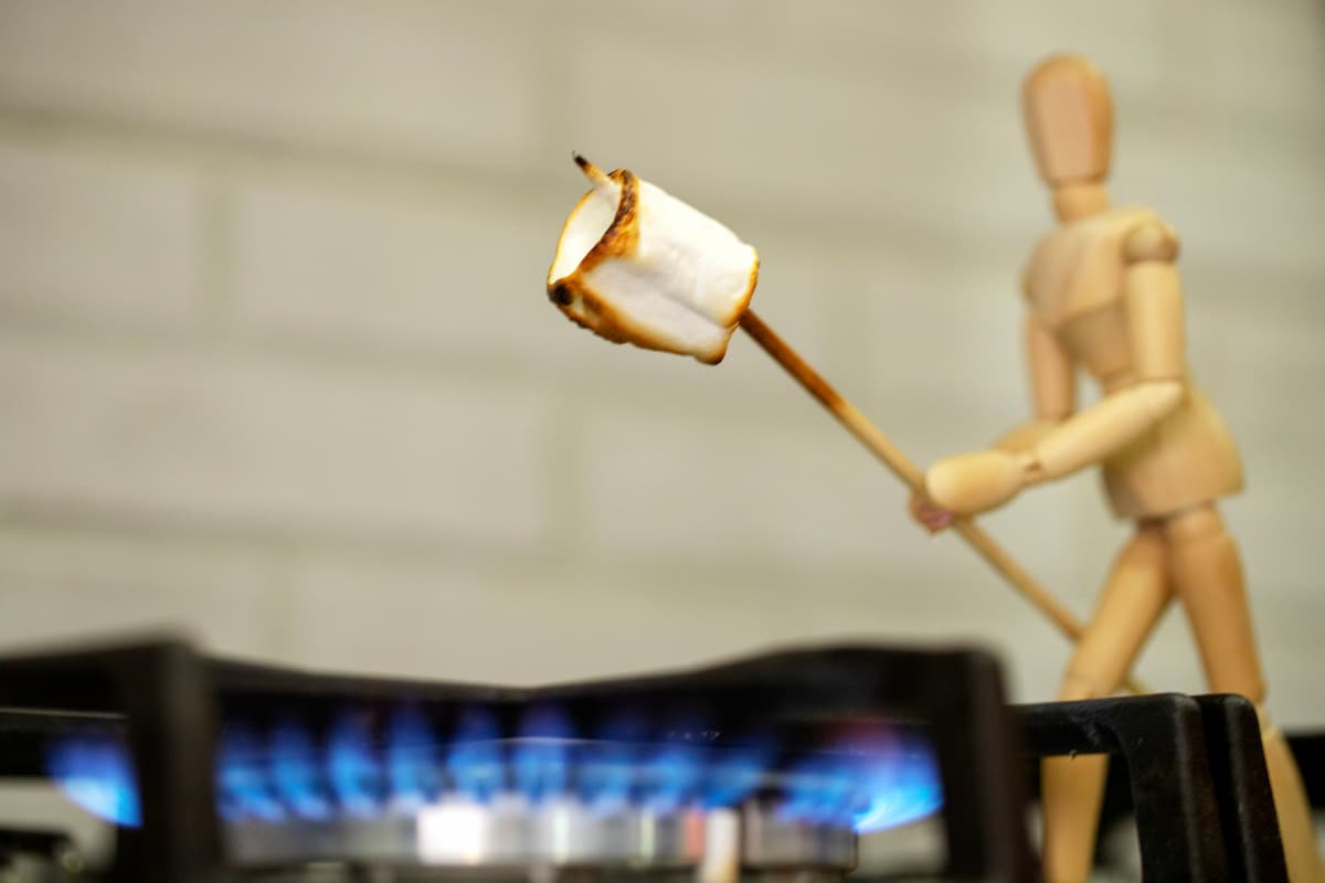 stick figure roasting marshmellow over gas fire on stove