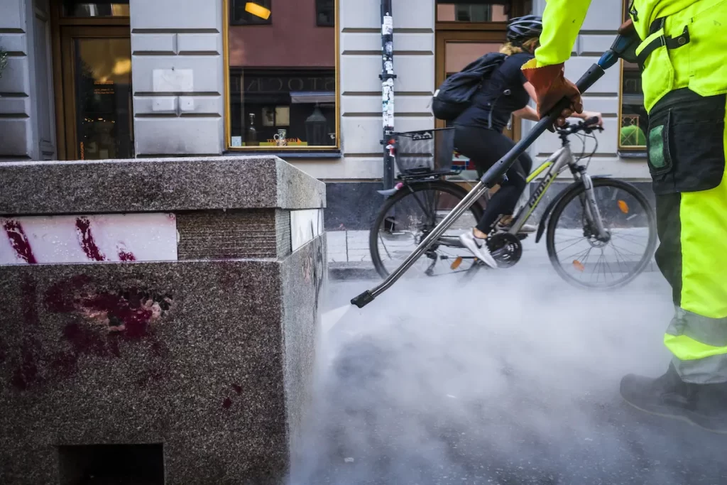 High pressured pressure washer using hot water to clean graffiti on street