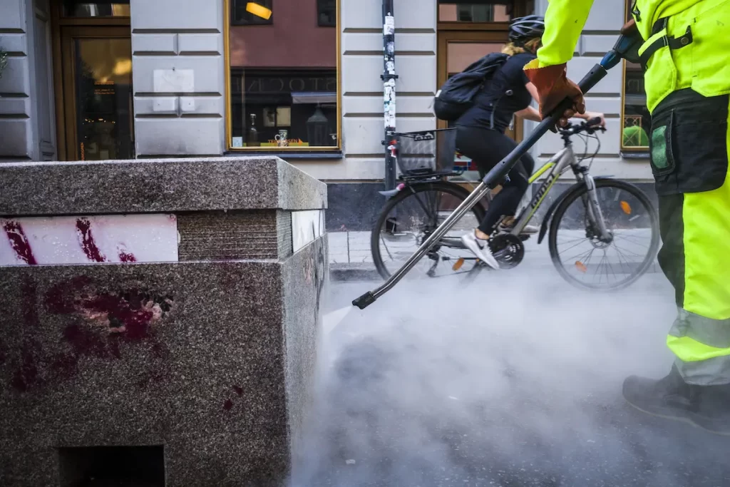 Sample of a man using hot water in a pressure washer to clean graffiti on street.