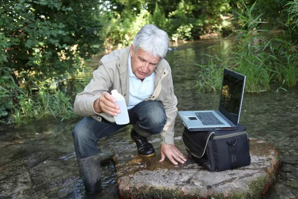 Close up of wildlife biologists working with water sample and laptop on edge of river