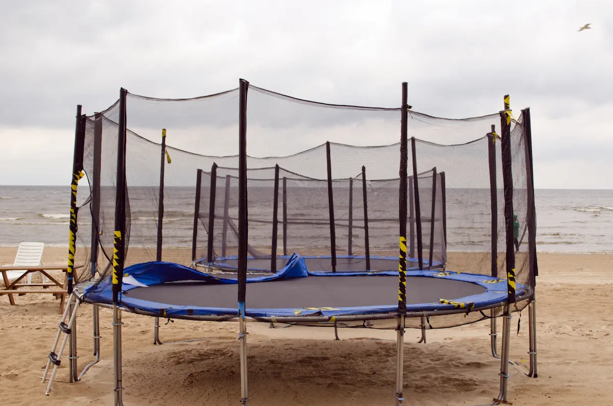 trampolines with net on beach with water in background