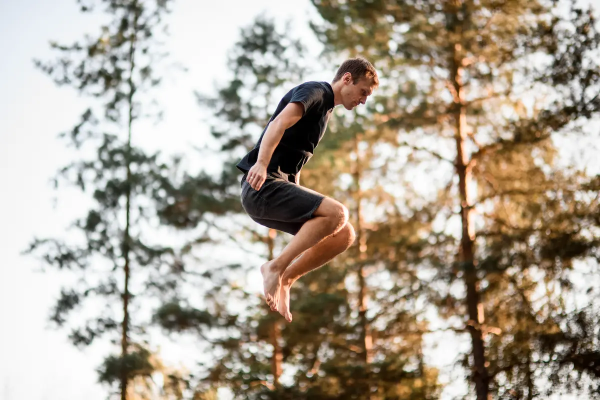 man in forest jumping on trampoline mid-air