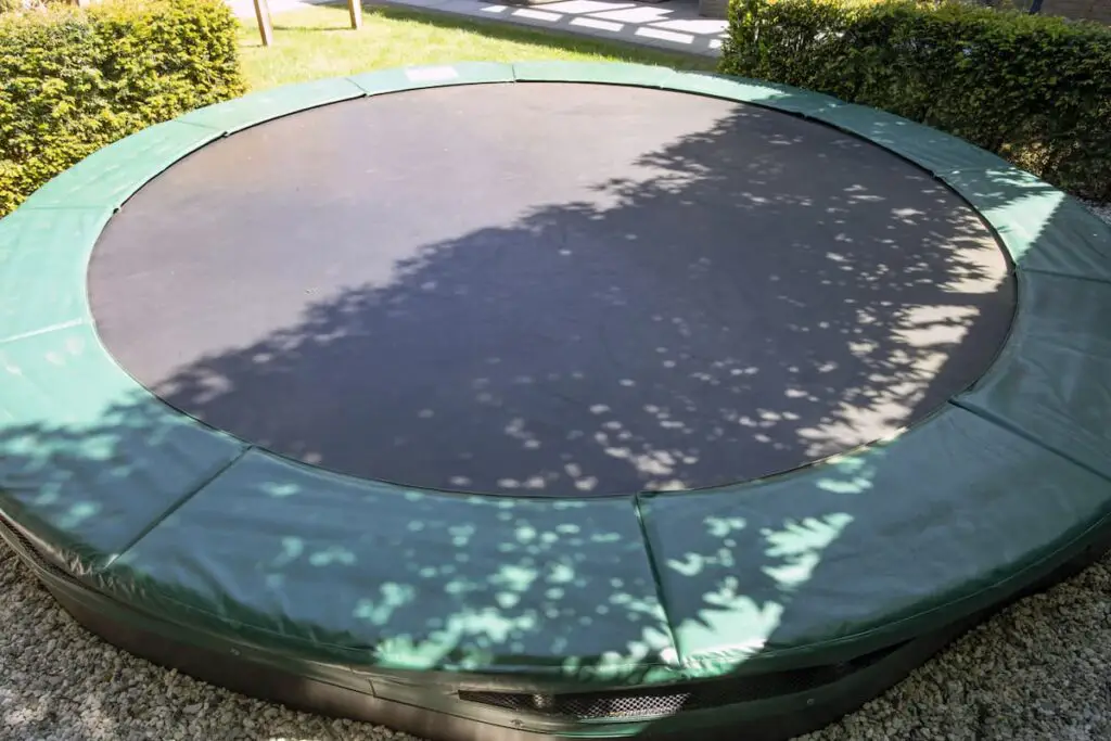 Green trampoline on the lawn in garden close-up empty as an example of trampoline use and scoliosis.  