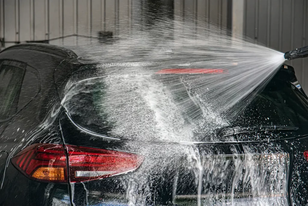 A car being cleaned at home with car wash soap in a pressure washer.