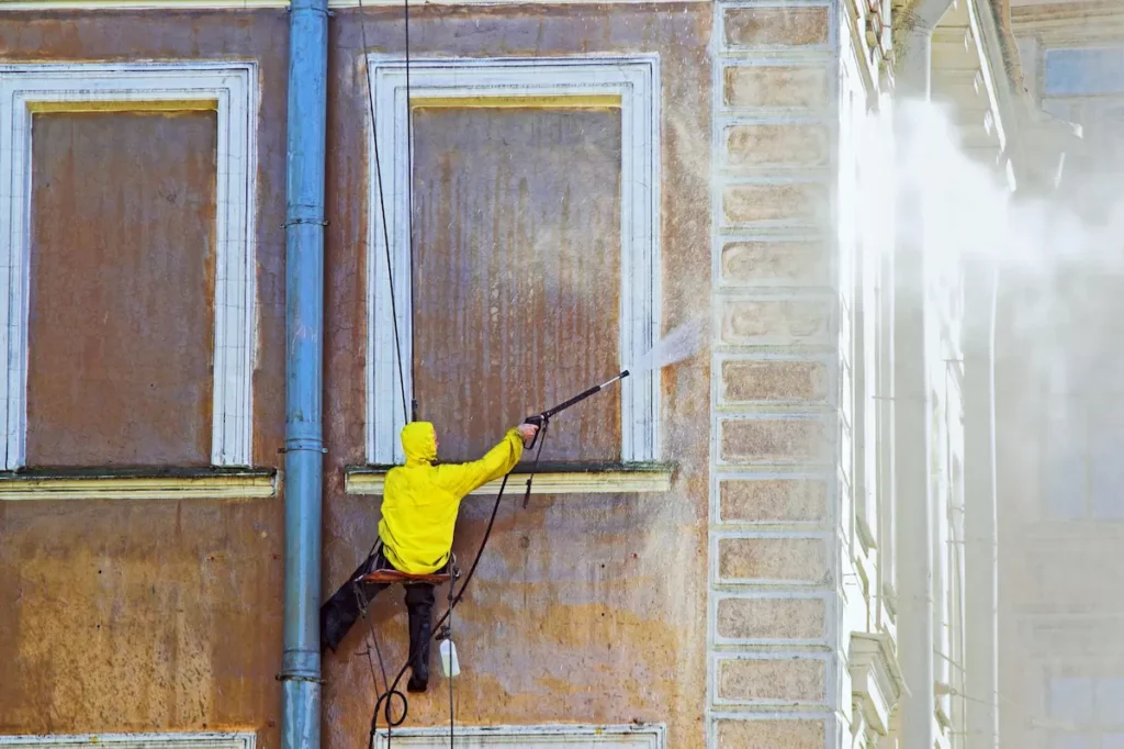 Man pressure washing side of buidling on scaffolding