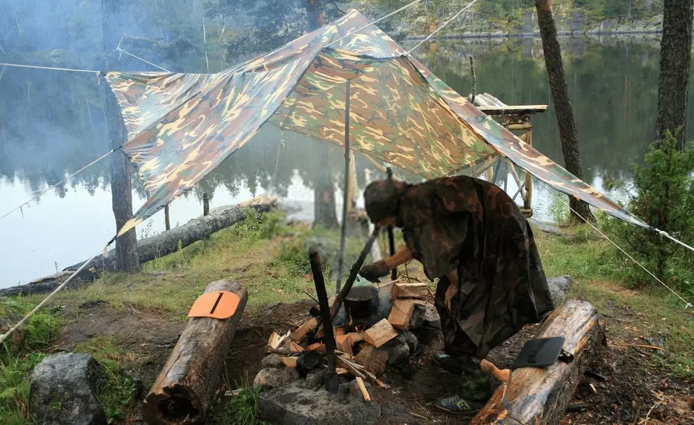 A man using a tarp shelter while wet weather camping.